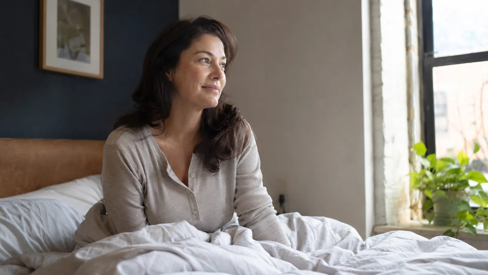 Person sitting up refreshed in bed in the morning, sunlight coming through the window